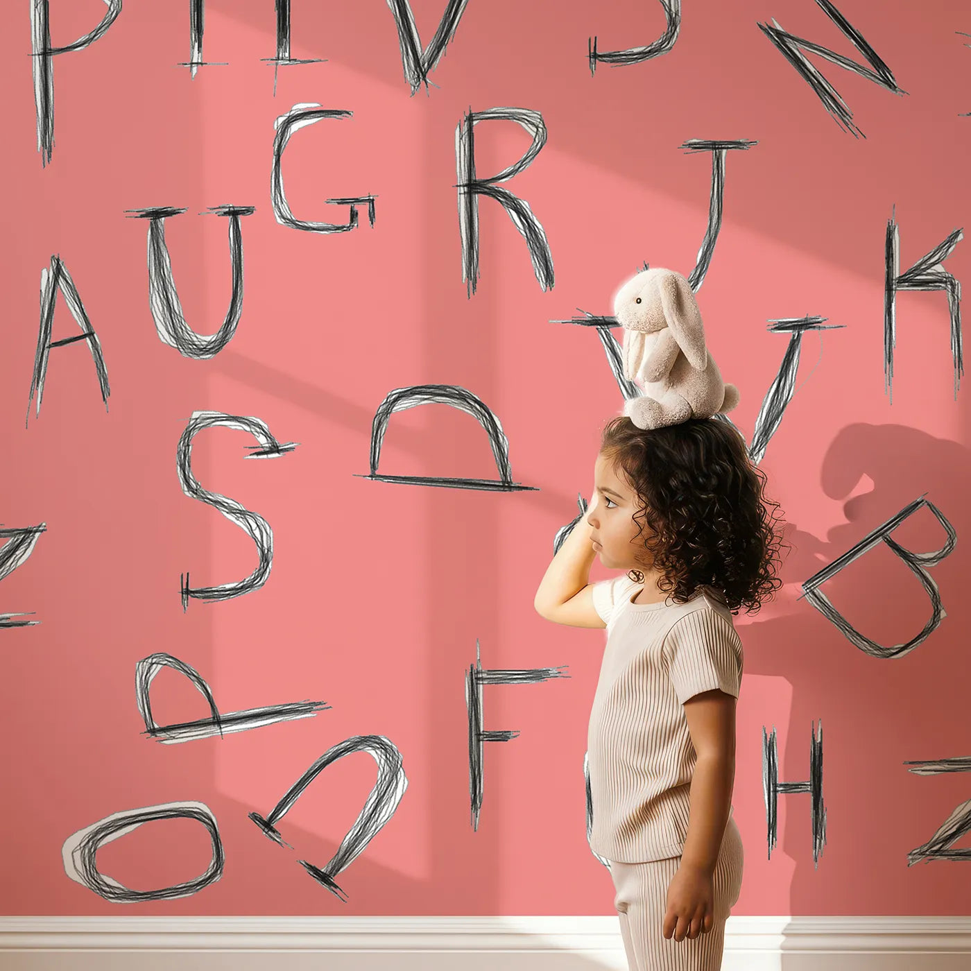 Child in front of Whimsy Tots Scattered Letters Wall Mural in Pink with alphabet, letter, abc, typography, learn, reading, sketch in design.