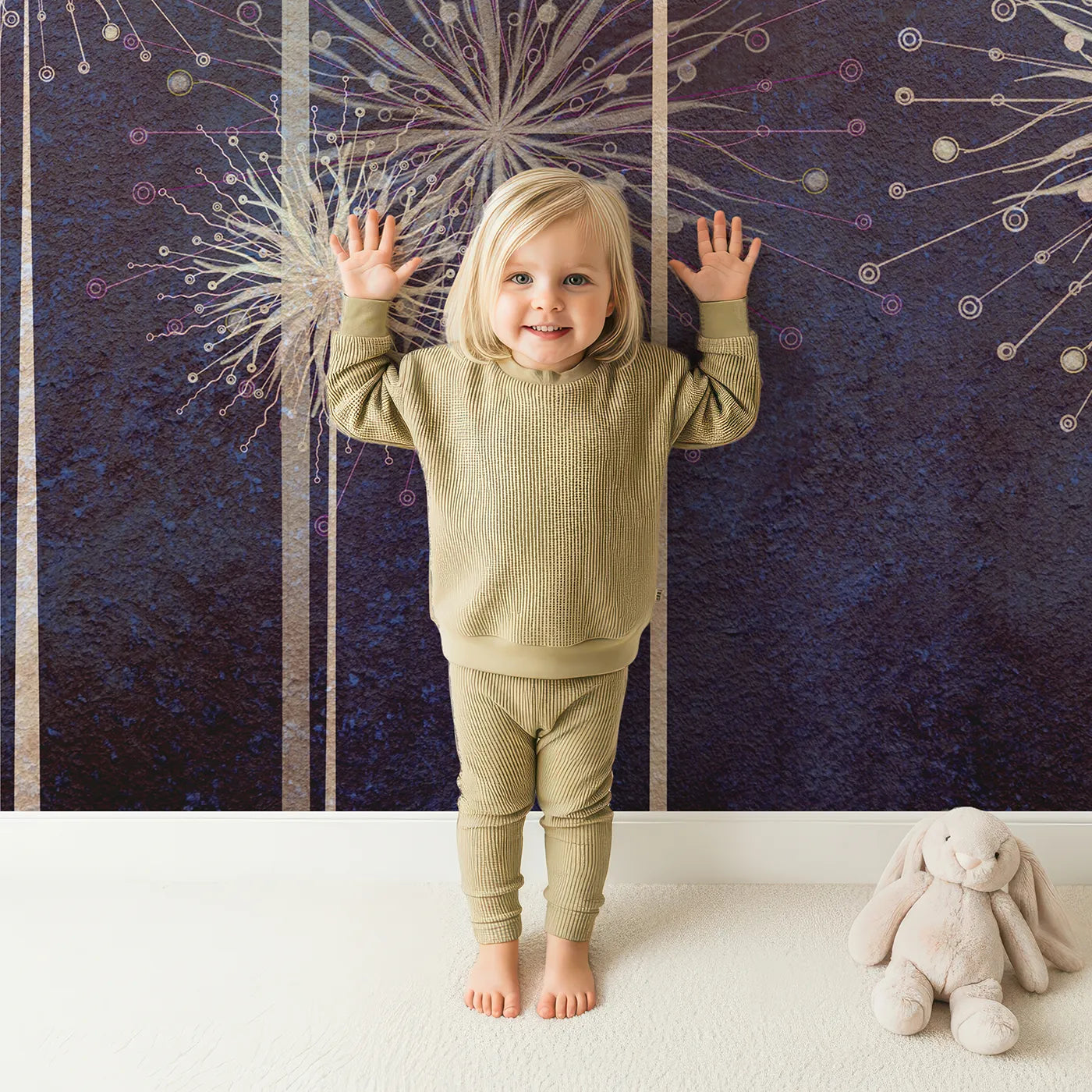 Child in front of Whimsy Tots Cosmic Dandelions Wall Mural with dandelion, firework, space, star, flower, abstract, dark, blue in design.