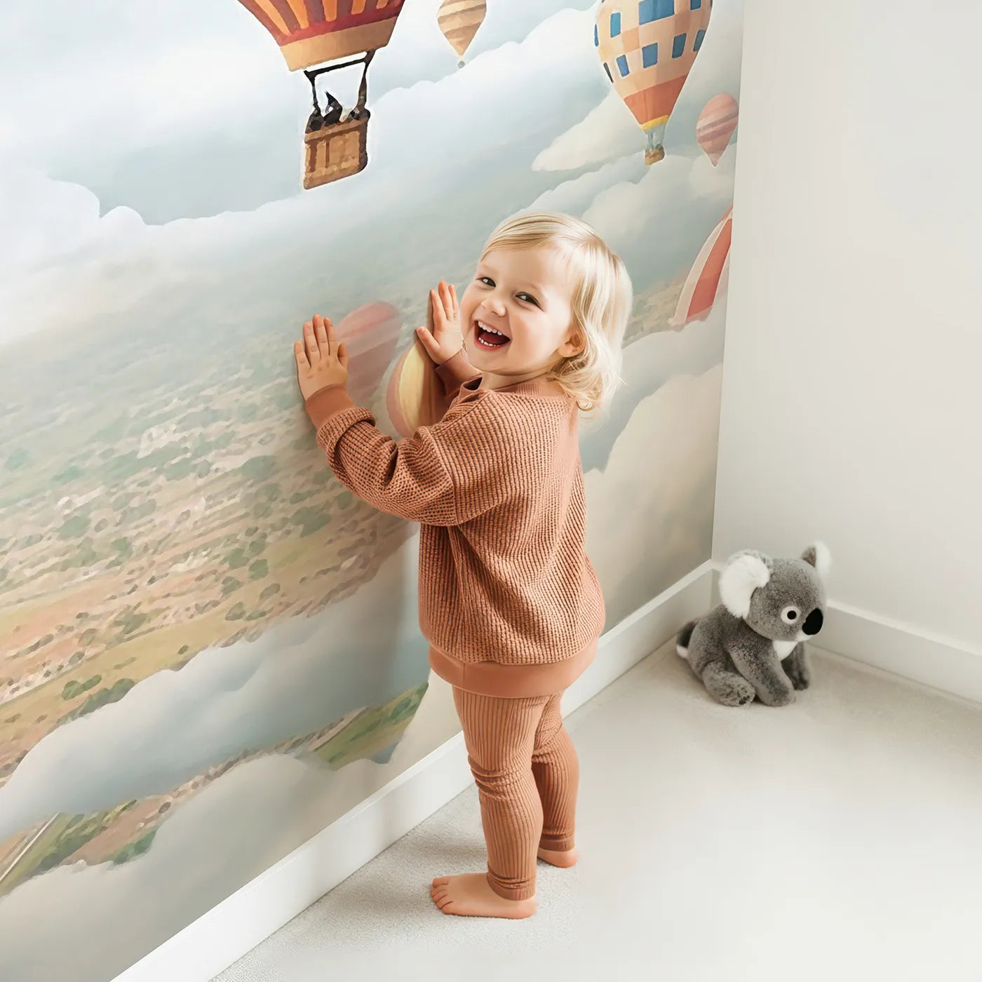 Child in front of Whimsy Tots Hot Air Balloon Rally Wall Mural with hot air balloon, balloon, sky, colorful, festival, adventure, town, clouds in design.
