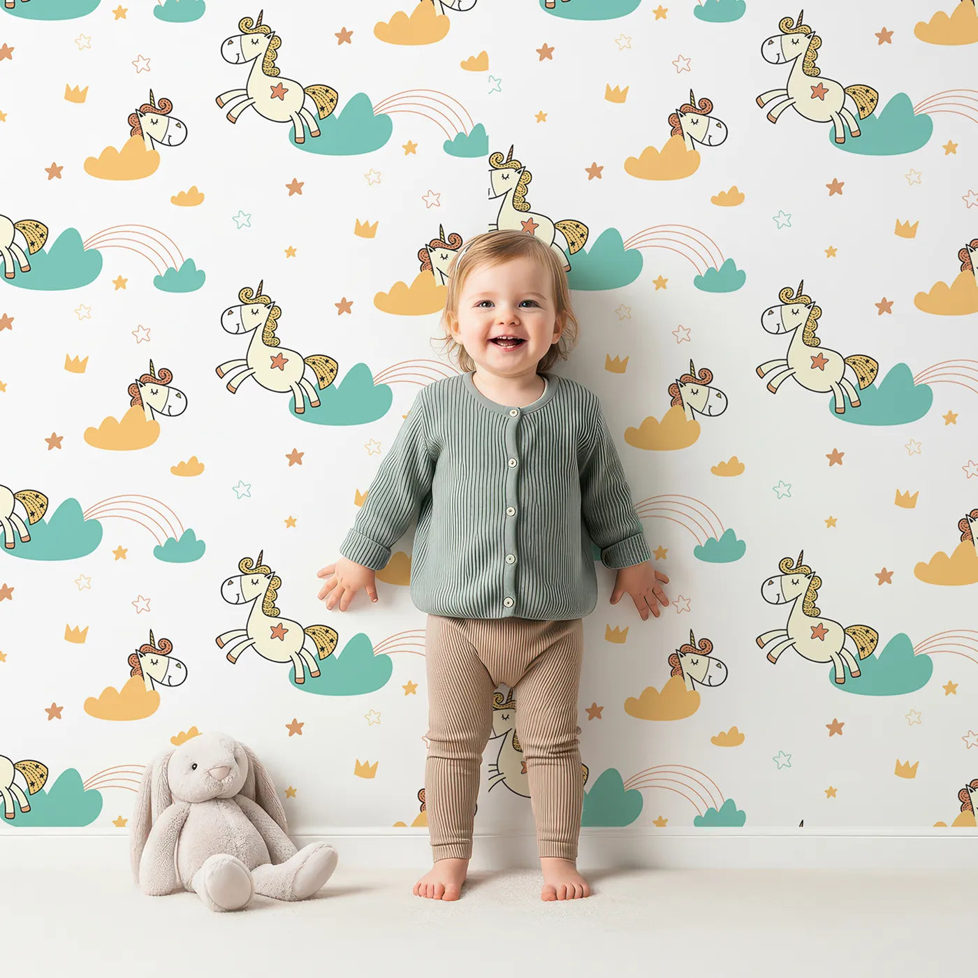 Lovely child standing in front of Whimsy Tots Unicorn Rainbow Cloud Wallpaper with unicorn, rainbow, cloud, star, crown in design.