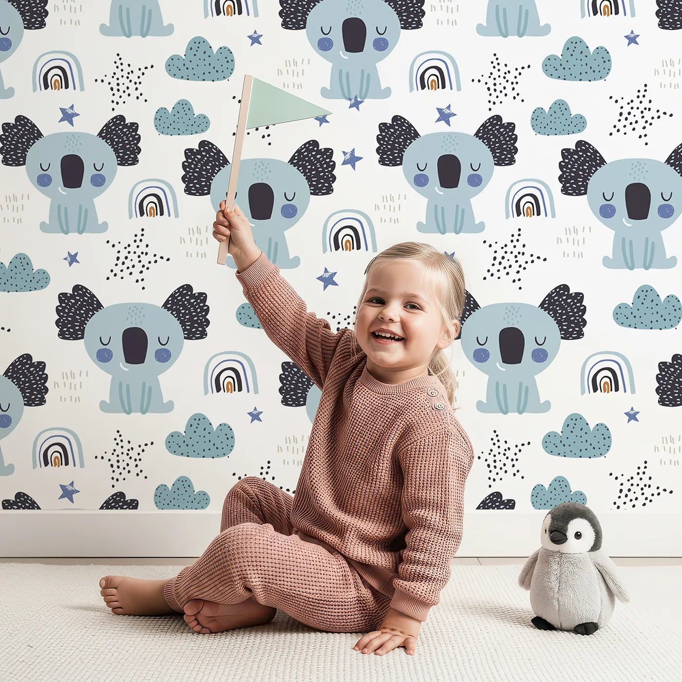 Lovely child standing in front of Whimsy Tots Sleepy Koala Rainbows Wallpaper with koala, rainbow, cloud, star, sleepy in design.