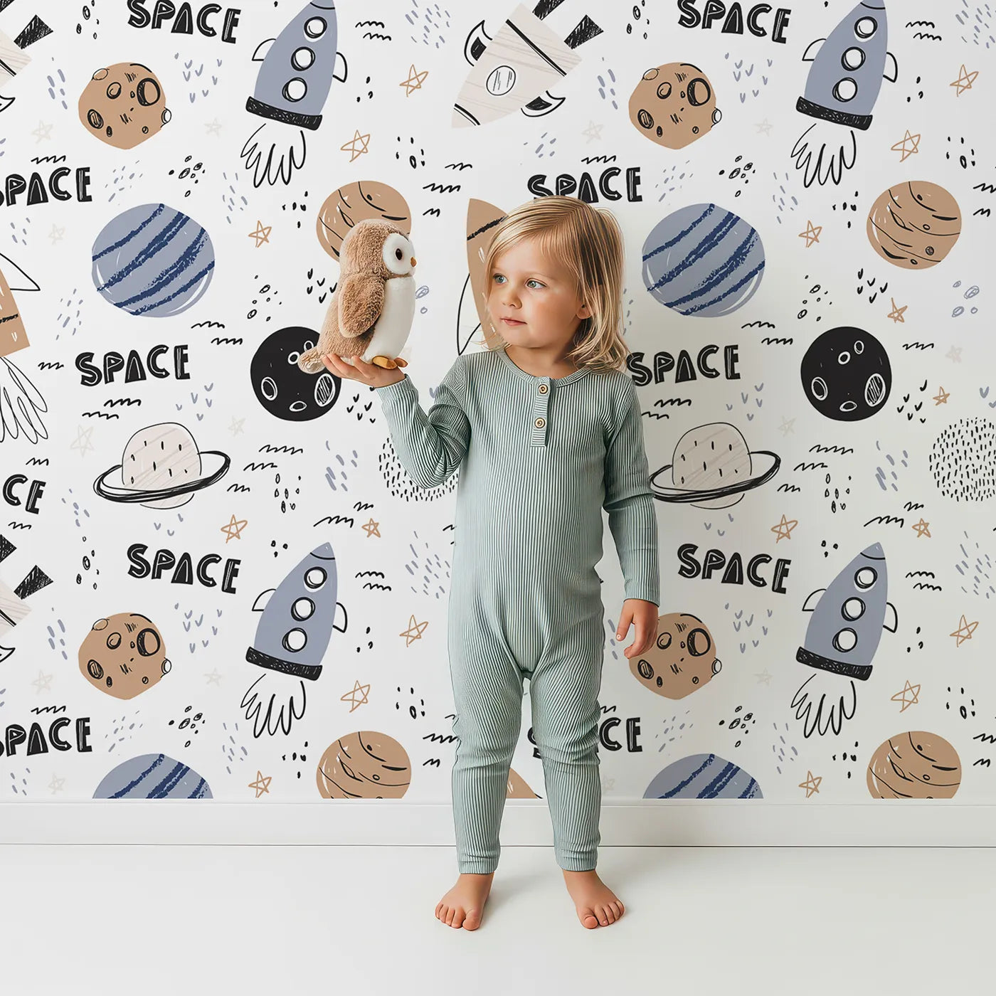 Lovely child standing in front of Whimsy Tots Boho Space Scribbles Wallpaper with space, rocket, planet, doodle, scandinavian in design.