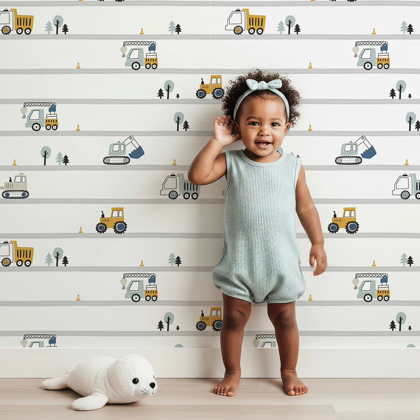 Lovely child standing in front of Whimsy Tots Busy Builders Roadway Wallpaper with construction, truck, road, excavator, tractor in design.