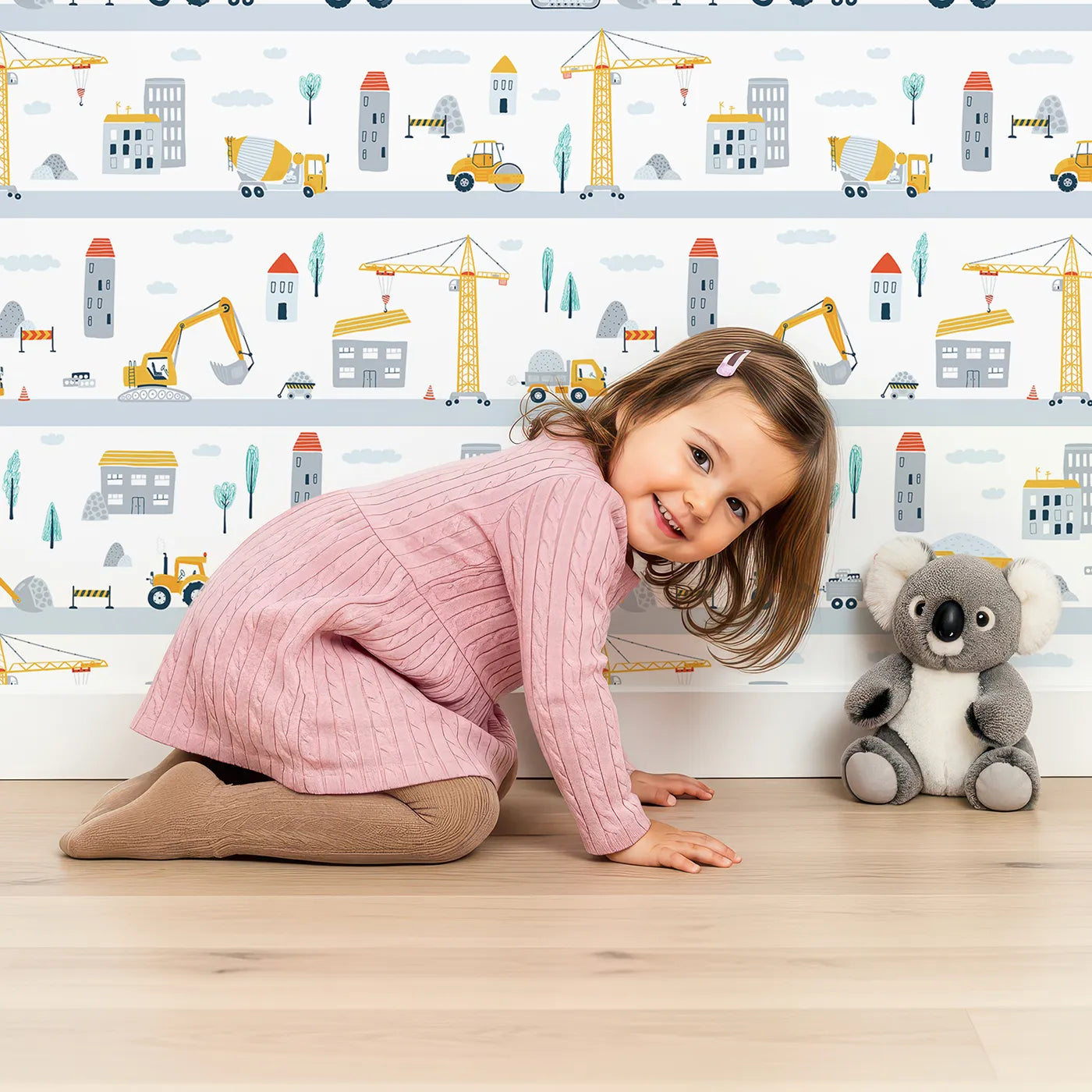 Lovely child standing in front of Whimsy Tots Busy City Builders Wallpaper with construction, city, truck, crane, building in design.