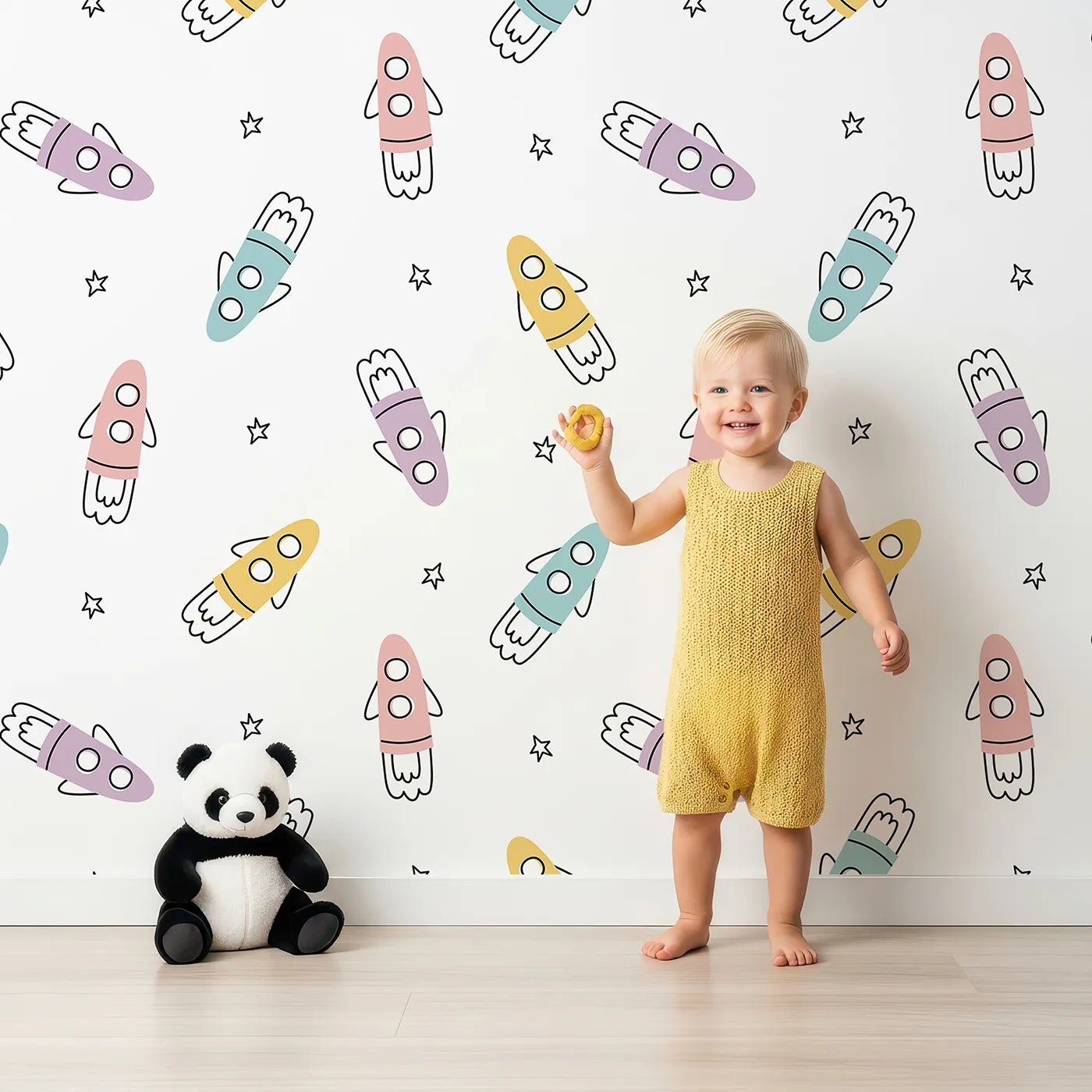 Lovely child standing in front of Whimsy Tots Pastel Doodle Rockets Wallpaper with rocket, space, star, pastel, doodle in design.