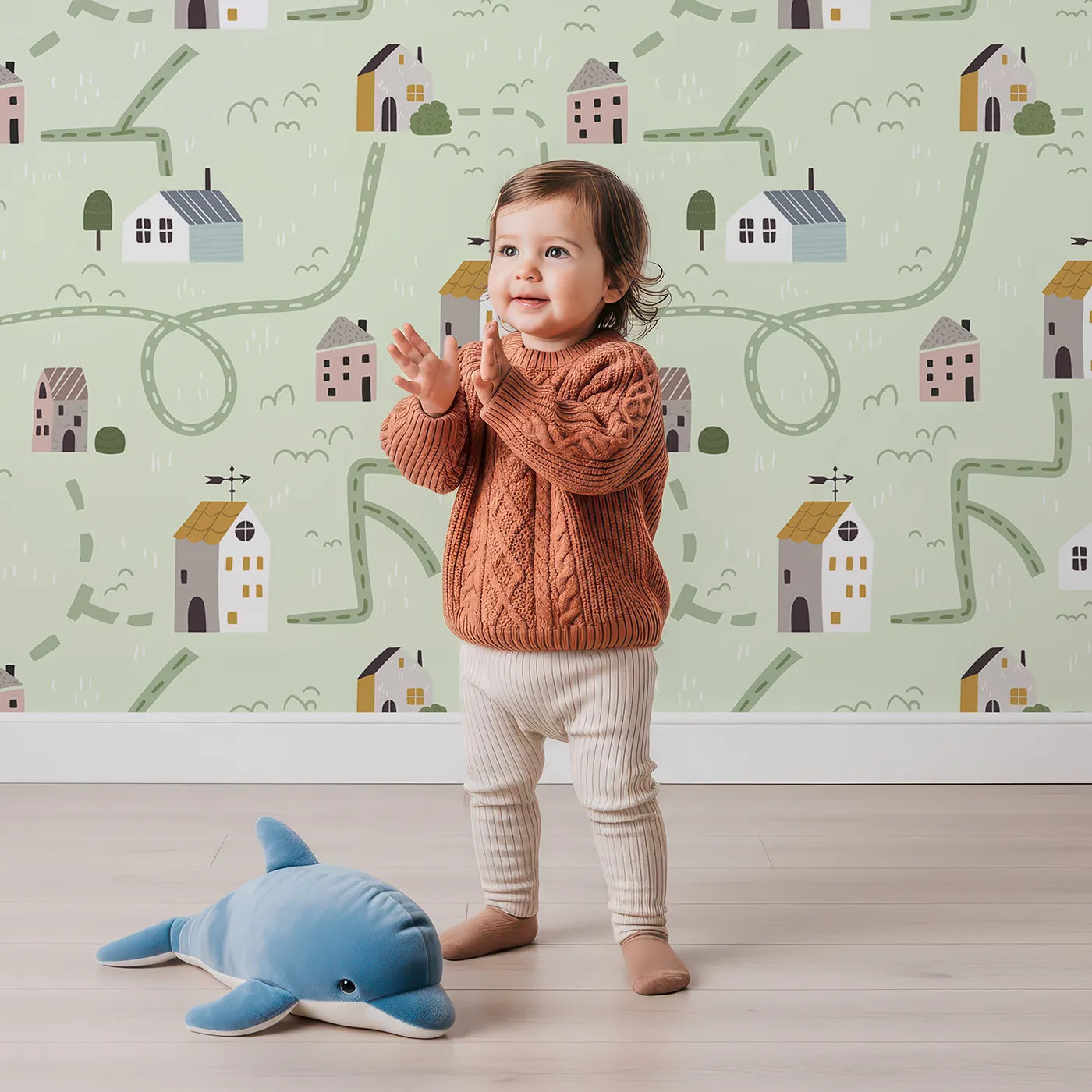 Lovely child standing in front of Whimsy Tots Winding Roads Village Map Wallpaper with map, road, house, village, city in design.
