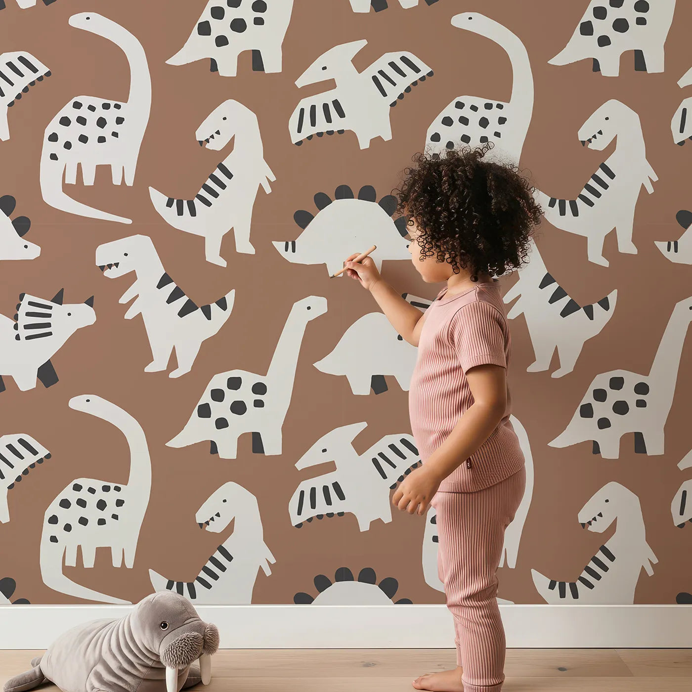 Lovely child standing in front of Whimsy Tots Paper Cut Dino Land Wallpaper in Brown with dinosaur, paper cut, modern, brown, silhouette in design.