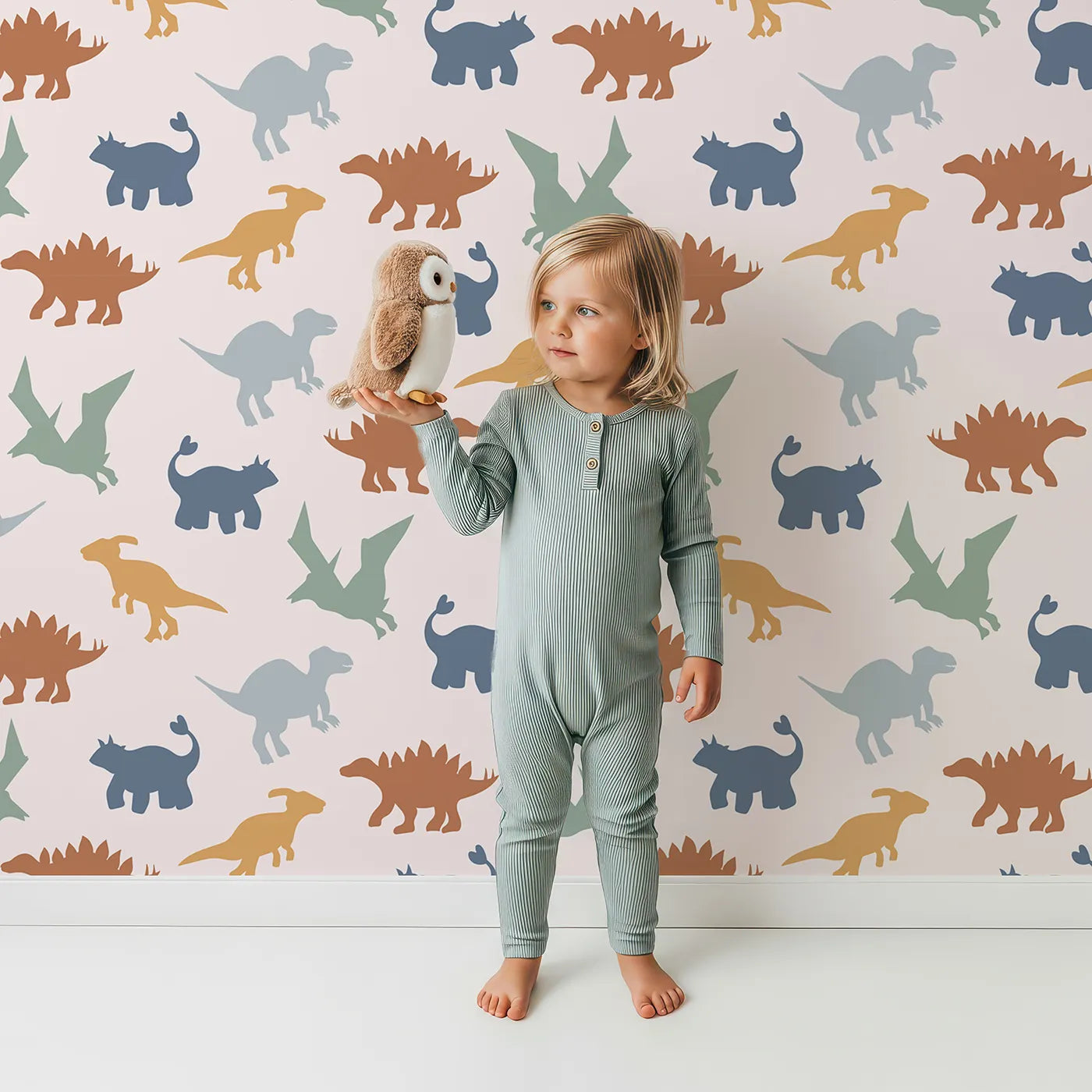 Lovely child standing in front of Whimsy Tots Earthy Dino Silhouettes Wallpaper with dinosaur, silhouette, earth tone, modern, neutral in design.