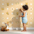 Lovely child standing in front of Whimsy Tots Buzzberry Bee Parade Wallpaper in Yellow with bee, flower, daisy, dot in design. Lovely child standing in front of Whimsy Tots Buzzberry Bee Parade Wallpaper in Yellow with bee, flower, daisy, dot in design.