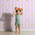 Lovely child standing in front of Whimsy Tots Daisy Lane Stripe Wallpaper in Purple with daisy, flower, stripe in design. Lovely child standing in front of Whimsy Tots Daisy Lane Stripe Wallpaper in Purple with daisy, flower, stripe in design.