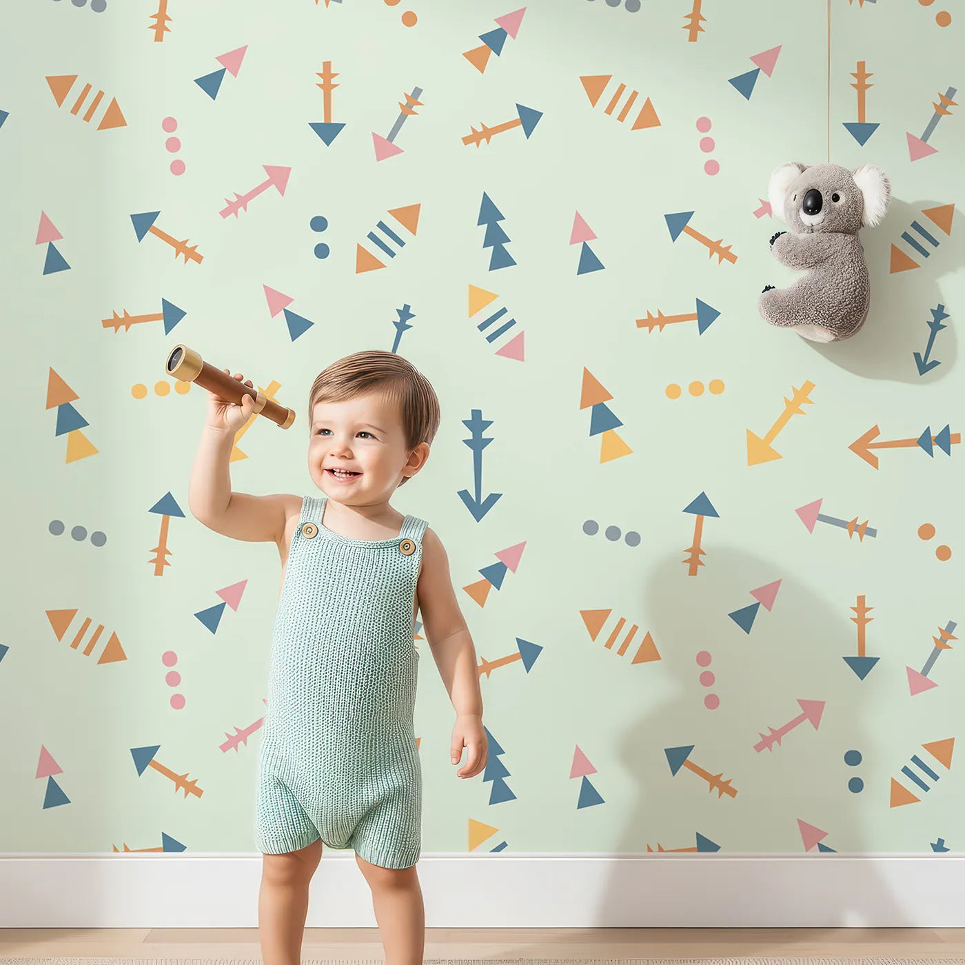 Lovely child standing in front of Whimsy Tots Boho Arrows Wallpaper in Mint Green with arrow, triangle, dot in design.