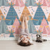 Lovely child standing in front of Whimsy Tots Teepee Parade Wallpaper in Pink with teepee, arrow, triangle, tent in design. Lovely child standing in front of Whimsy Tots Teepee Parade Wallpaper in Pink with teepee, arrow, triangle, tent in design.