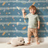 Lovely child standing in front of Whimsy Tots Tribal Sky Dance Wallpaper with arrow, feather, star, stripe in design. Lovely child standing in front of Whimsy Tots Tribal Sky Dance Wallpaper with arrow, feather, star, stripe in design.