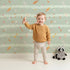 Lovely child standing in front of Whimsy Tots Tribal Sky Dance Wallpaper in Green with arrow, feather, star, stripe in design. Lovely child standing in front of Whimsy Tots Tribal Sky Dance Wallpaper in Green with arrow, feather, star, stripe in design.