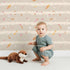 Lovely child standing in front of Whimsy Tots Tribal Sky Dance Wallpaper in Beige with arrow, feather, star, stripe in design. Lovely child standing in front of Whimsy Tots Tribal Sky Dance Wallpaper in Beige with arrow, feather, star, stripe in design.