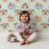 Lovely child standing in front of Whimsy Tots Woodland Royalty Parade Wallpaper in Mint Green with bear, deer, elephant, tiger, feather, wreath, crown in design. Lovely child standing in front of Whimsy Tots Woodland Royalty Parade Wallpaper in Mint Green with bear, deer, elephant, tiger, feather, wreath, crown in design.