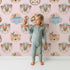 Lovely child standing in front of Whimsy Tots Woodland Royalty Parade Wallpaper in Pink with bear, deer, elephant, tiger, feather, wreath, crown in design. Lovely child standing in front of Whimsy Tots Woodland Royalty Parade Wallpaper in Pink with bear, deer, elephant, tiger, feather, wreath, crown in design.