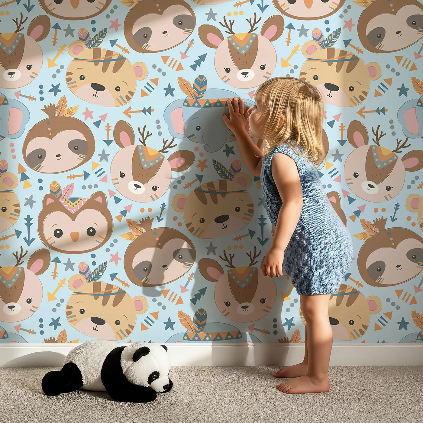 Lovely child standing in front of Whimsy Tots Wild Whimsy Tribe Wallpaper in Blue with bear, deer, elephant, tiger, owl, sloth, arrow, feather, star in design.