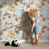 Lovely child standing in front of Whimsy Tots Wild Whimsy Tribe Wallpaper in Blue with bear, deer, elephant, tiger, owl, sloth, arrow, feather, star in design. Lovely child standing in front of Whimsy Tots Wild Whimsy Tribe Wallpaper in Blue with bear, deer, elephant, tiger, owl, sloth, arrow, feather, star in design.