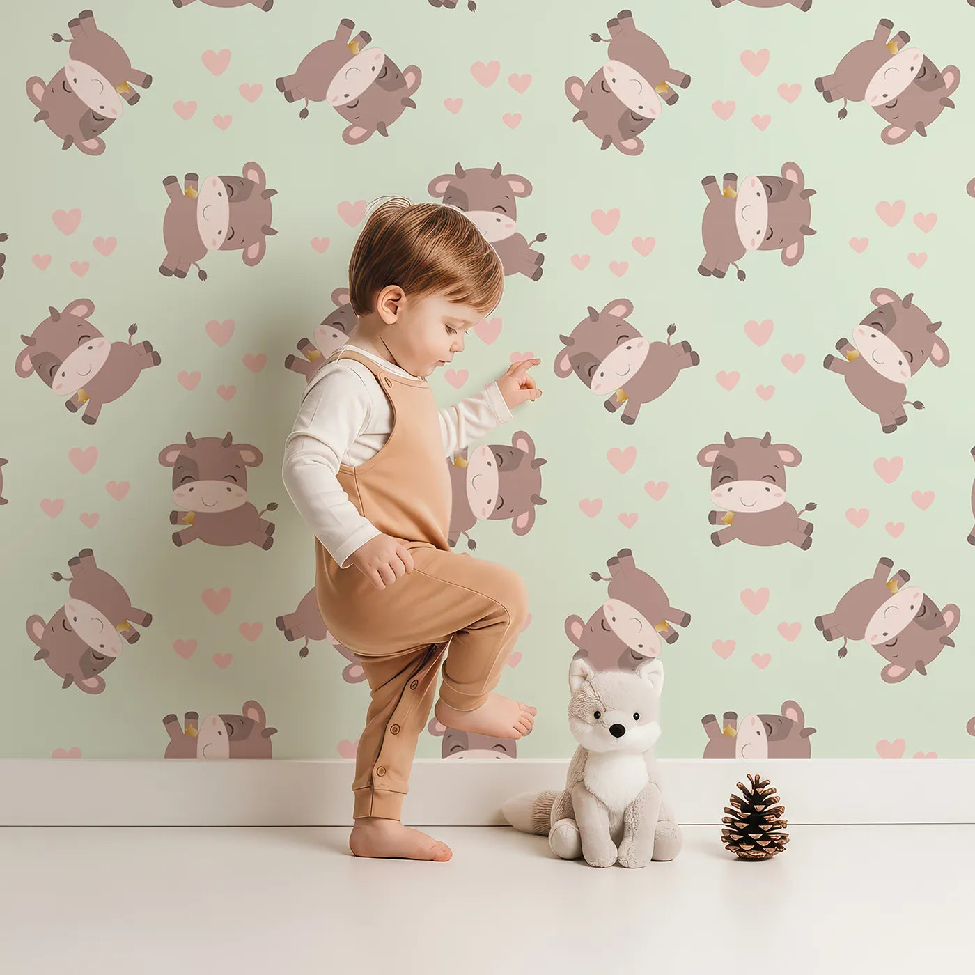Lovely child standing in front of Whimsy Tots Moo Moo Love Wallpaper in Mint Green with cow, heart, bell in design.