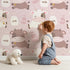 Lovely child standing in front of Whimsy Tots Moo Moo Milk Parade Wallpaper in Pink with cow, bottle, bell, dot in design. Lovely child standing in front of Whimsy Tots Moo Moo Milk Parade Wallpaper in Pink with cow, bottle, bell, dot in design.