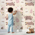 Lovely child standing in front of Whimsy Tots Moo Moo Milk Parade Wallpaper in Cream with cow, bottle, bell, dot in design. Lovely child standing in front of Whimsy Tots Moo Moo Milk Parade Wallpaper in Cream with cow, bottle, bell, dot in design.