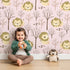 Lovely child standing in front of Whimsy Tots Little Lion Nap Wallpaper in Pink with lion, tree, footprint in design. Lovely child standing in front of Whimsy Tots Little Lion Nap Wallpaper in Pink with lion, tree, footprint in design.
