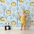 Lovely child standing in front of Whimsy Tots Little Lion Nap Wallpaper in Blue with lion, tree, footprint in design. Lovely child standing in front of Whimsy Tots Little Lion Nap Wallpaper in Blue with lion, tree, footprint in design.