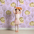 Lovely child standing in front of Whimsy Tots Little Lion Nap Wallpaper in Purple with lion, tree, footprint in design. Lovely child standing in front of Whimsy Tots Little Lion Nap Wallpaper in Purple with lion, tree, footprint in design.