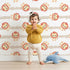 Lovely child standing in front of Whimsy Tots Striped Safari Cubs Wallpaper in Beige with lion, stripe, paw in design. Lovely child standing in front of Whimsy Tots Striped Safari Cubs Wallpaper in Beige with lion, stripe, paw in design.