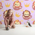 Lovely child standing in front of Whimsy Tots Little King of the Jungle Wallpaper in Purple with lion, crown, teacup in design. Lovely child standing in front of Whimsy Tots Little King of the Jungle Wallpaper in Purple with lion, crown, teacup in design.