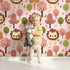 Lovely child standing in front of Whimsy Tots Autumn Safari Stroll Wallpaper in Pink with lion, tree, leaf in design. Lovely child standing in front of Whimsy Tots Autumn Safari Stroll Wallpaper in Pink with lion, tree, leaf in design.