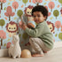 Lovely child standing in front of Whimsy Tots Autumn Safari Stroll Wallpaper in Blue with lion, tree, leaf in design. Lovely child standing in front of Whimsy Tots Autumn Safari Stroll Wallpaper in Blue with lion, tree, leaf in design.
