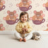 Lovely child standing in front of Whimsy Tots Lovely Tea Mice Wallpaper in Cream with mouse, cup, sprinkle in design. Lovely child standing in front of Whimsy Tots Lovely Tea Mice Wallpaper in Cream with mouse, cup, sprinkle in design.