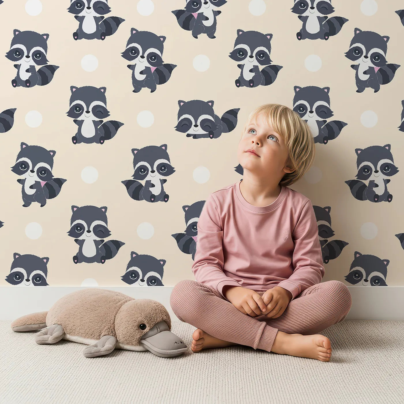 Lovely child standing in front of Whimsy Tots Playful Raccoon Parade Wallpaper in Cream with raccoon, dot in design.