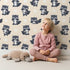 Lovely child standing in front of Whimsy Tots Playful Raccoon Parade Wallpaper in Cream with raccoon, dot in design. Lovely child standing in front of Whimsy Tots Playful Raccoon Parade Wallpaper in Cream with raccoon, dot in design.