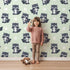 Lovely child standing in front of Whimsy Tots Playful Raccoon Parade Wallpaper in Green with raccoon, dot in design. Lovely child standing in front of Whimsy Tots Playful Raccoon Parade Wallpaper in Green with raccoon, dot in design.