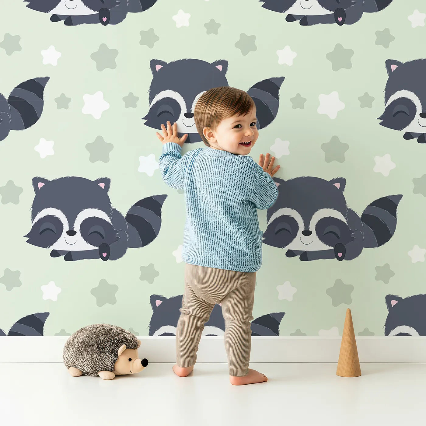 Lovely child standing in front of Whimsy Tots Raccoon Dream Stars Wallpaper in Green with raccoon, star in design.