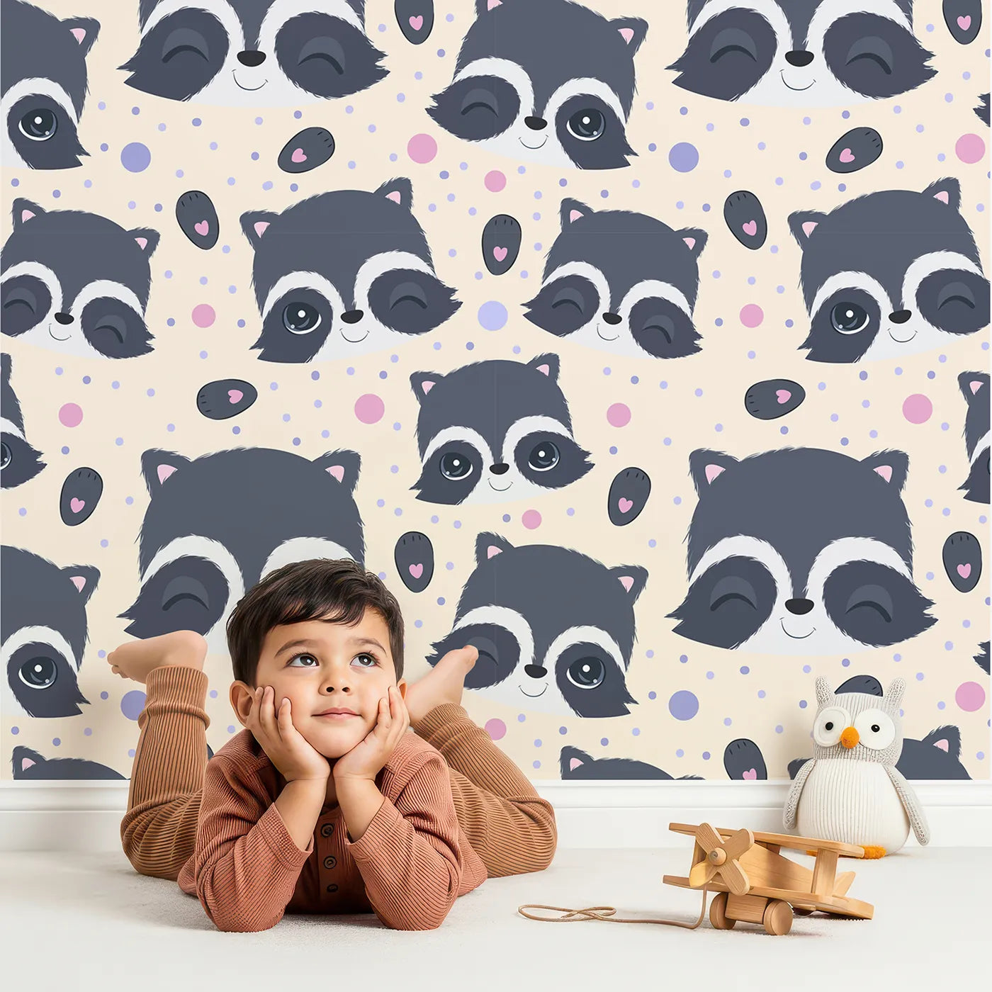 Lovely child standing in front of Whimsy Tots Winkie Raccoon Pals Wallpaper in Cream with raccoon, dot, paw in design.