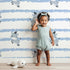 Lovely child standing in front of Whimsy Tots Winkie the Zebra Wallpaper in Blue with zebra, stripe in design. Lovely child standing in front of Whimsy Tots Winkie the Zebra Wallpaper in Blue with zebra, stripe in design.