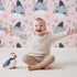 Lovely child standing in front of Whimsy Tots Zebra Snuggle Smiles Wallpaper in Blush Pink with zebra, heart, face in design. Lovely child standing in front of Whimsy Tots Zebra Snuggle Smiles Wallpaper in Blush Pink with zebra, heart, face in design.