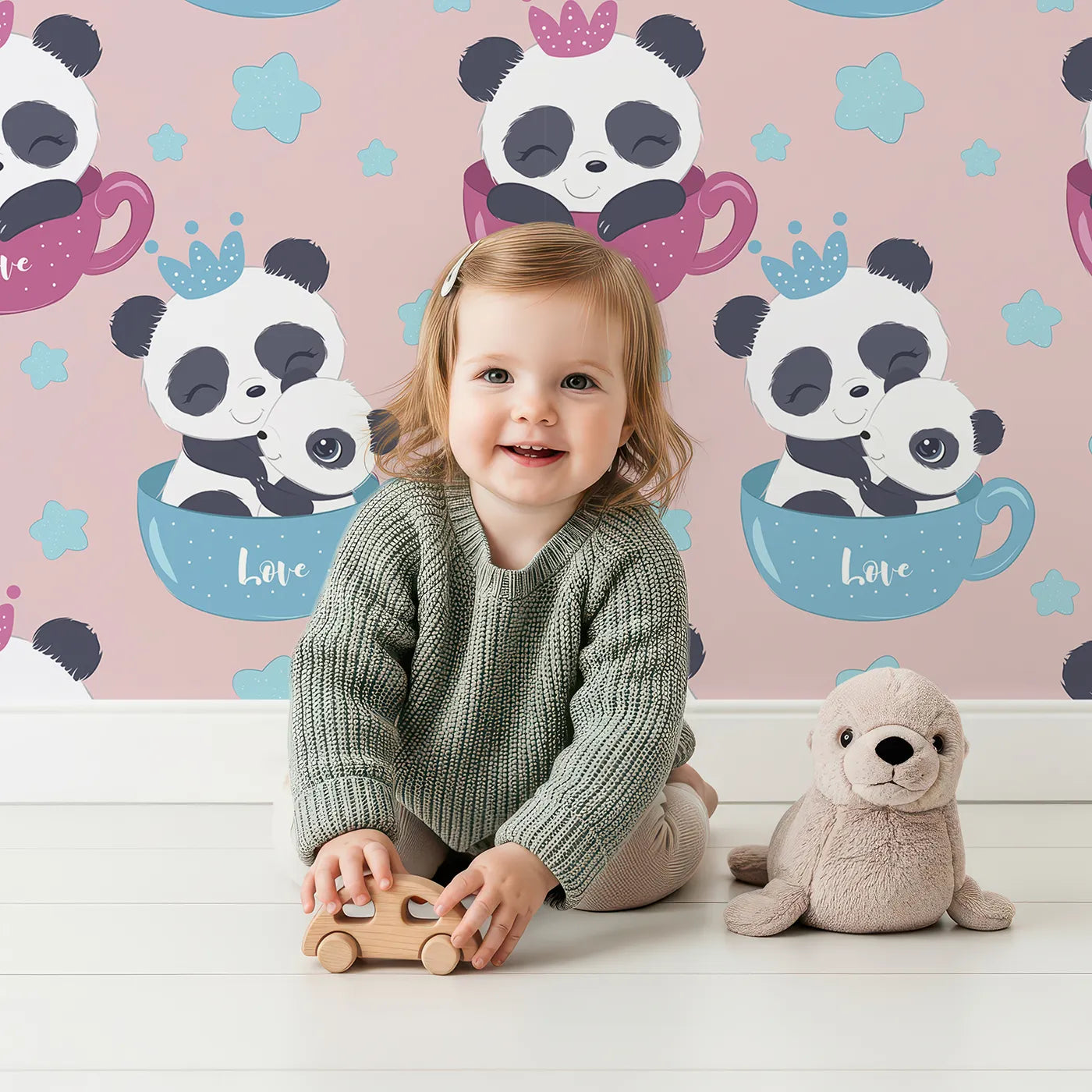 Lovely child standing in front of Whimsy Tots Cuddle Cup Panda Wallpaper in Pink with panda, cup, star, crown in design.