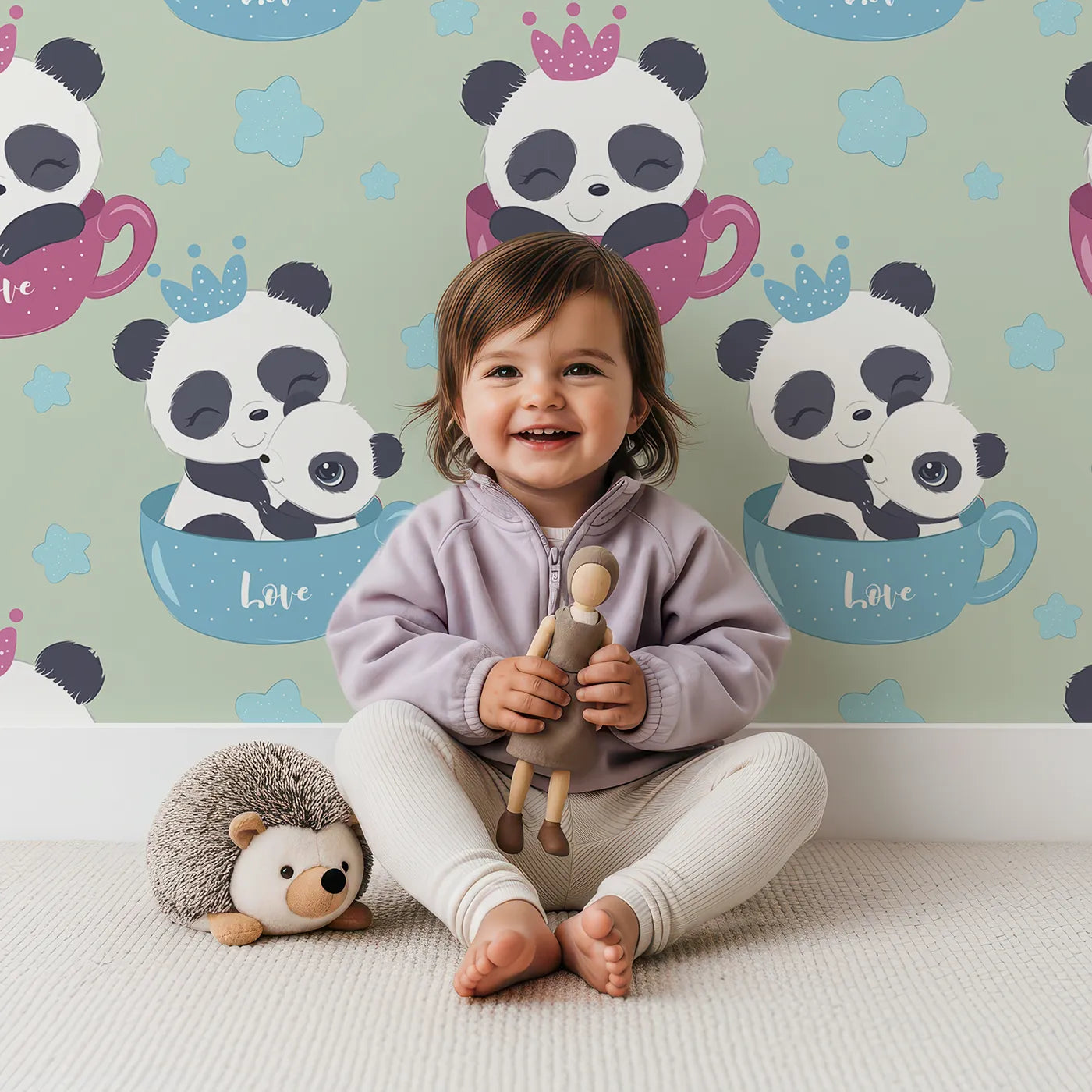Lovely child standing in front of Whimsy Tots Cuddle Cup Panda Wallpaper in Sage Green with panda, cup, star, crown in design.