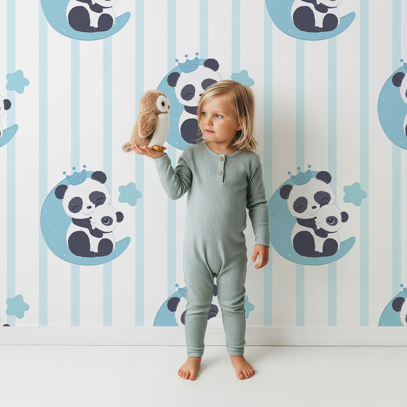Lovely child standing in front of Whimsy Tots Moon Cuddle Panda Wallpaper in Blue with panda, moon, star, stripe, crown in design.
