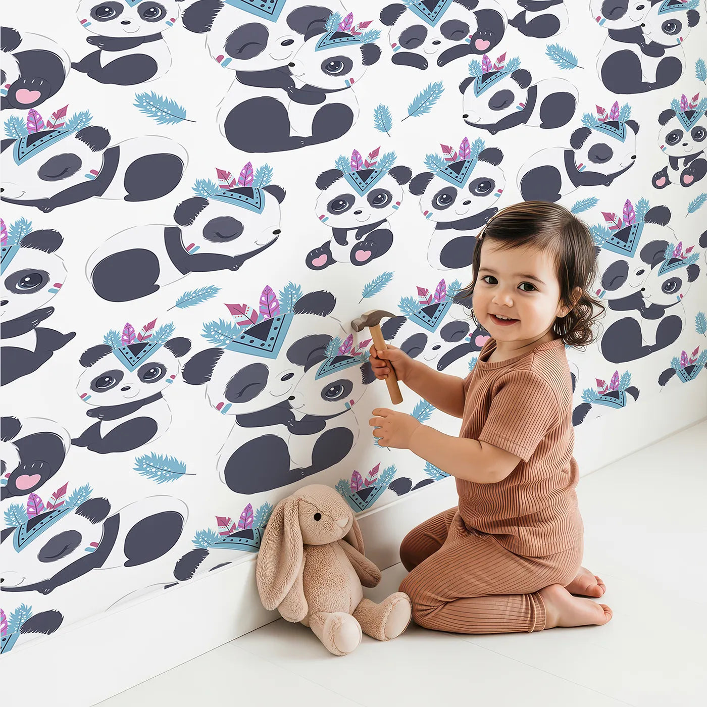 Lovely child standing in front of Whimsy Tots Tribal Hug Panda Wallpaper in White with panda, feather, headband, hug, leaf in design.