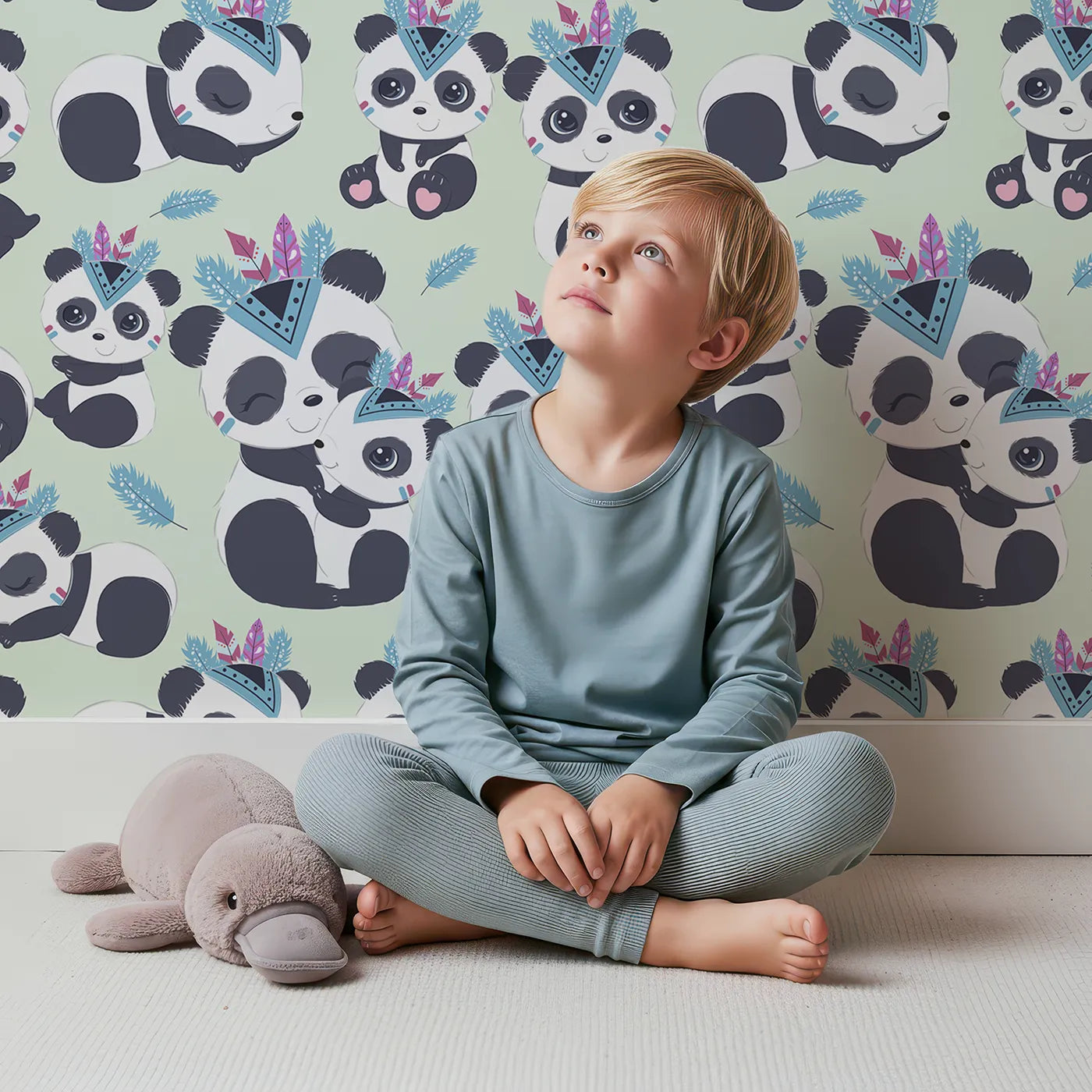 Lovely child standing in front of Whimsy Tots Tribal Hug Panda Wallpaper in Mint Green with panda, feather, headband, hug, leaf in design.