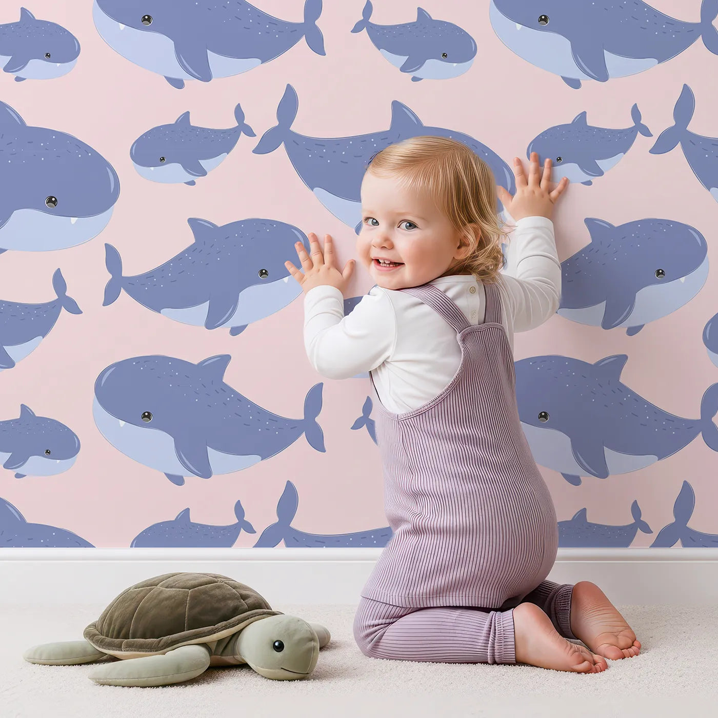 Lovely child standing in front of Whimsy Tots Whale Shark Wiggles Wallpaper in Blush Pink with shark, whale shark, spot, sea in design.
