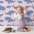 Lovely child standing in front of Whimsy Tots Whale Shark Wiggles Wallpaper in Blush Pink with shark, whale shark, spot, sea in design. Lovely child standing in front of Whimsy Tots Whale Shark Wiggles Wallpaper in Blush Pink with shark, whale shark, spot, sea in design.