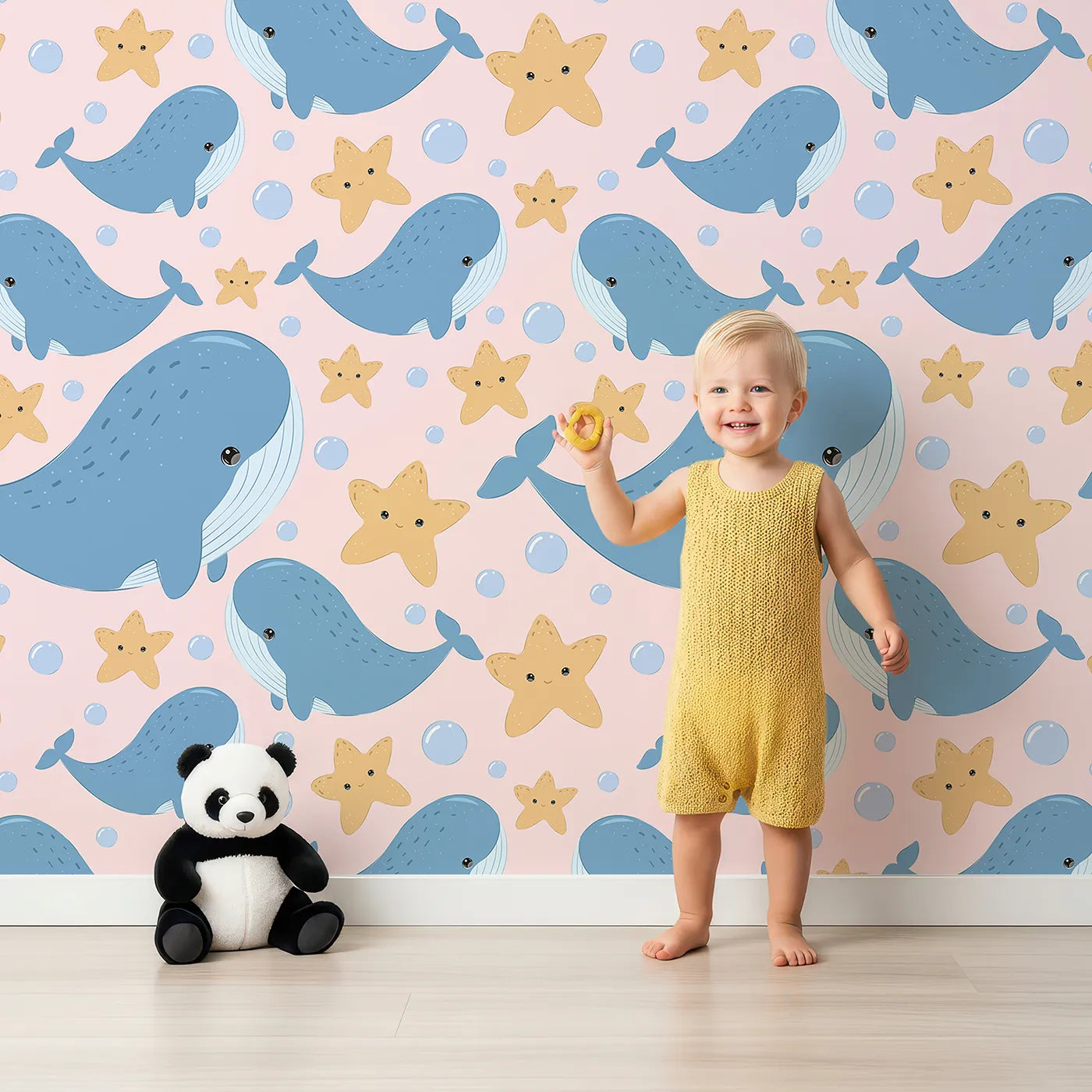 Lovely child standing in front of Whimsy Tots Starry Whale Friends Wallpaper in Blush Pink with whale, starfish, bubble, dot in design.