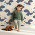 Lovely child standing in front of Whimsy Tots Orca Whale Wonder Wallpaper in Cream with whale, orca, bubble, wave in design. Lovely child standing in front of Whimsy Tots Orca Whale Wonder Wallpaper in Cream with whale, orca, bubble, wave in design.